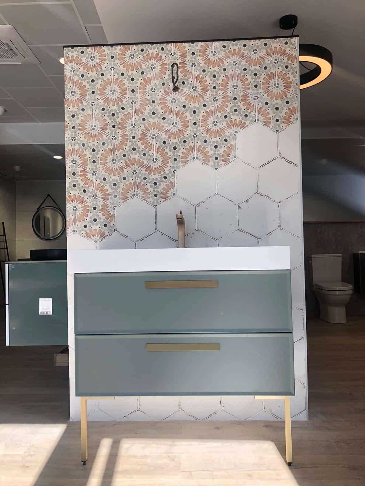 Mobilier de salle de bain avec deux tiroirs bleus sur pied, adossé à un panneau décoratif multicolore à motifs géométriques, dans un intérieur de toilettes.