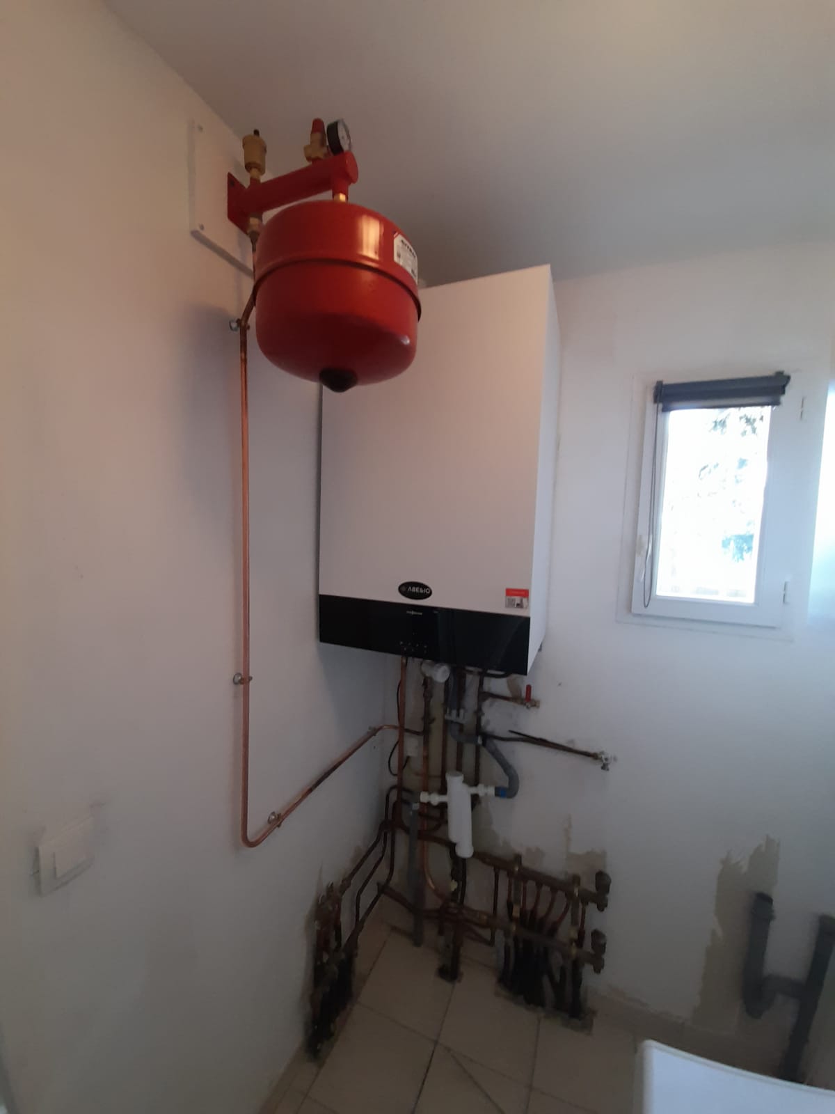 Chaudière et ballon d’eau chaude rouges avec tuyauteries et écran de contrôle au mur, dans une buanderie technique.