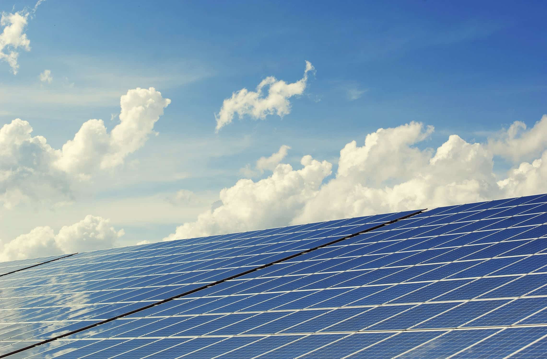 Toit recouvert de panneaux solaires bleus sous un ciel bleu avec de gros nuages blancs.