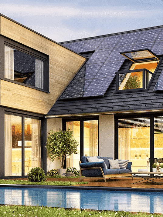 Vue extérieure moderne d’une maison avec panneaux solaires sur le toit, grande baie vitrée, terrasse et piscine bordée de végétation, au soleil.