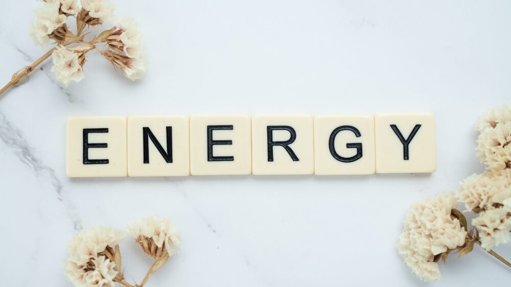 Boules de lettres en chocolat blanc alignées sur un fond clair, formant le mot ENERGY, entourées de fleurs séchées crème.