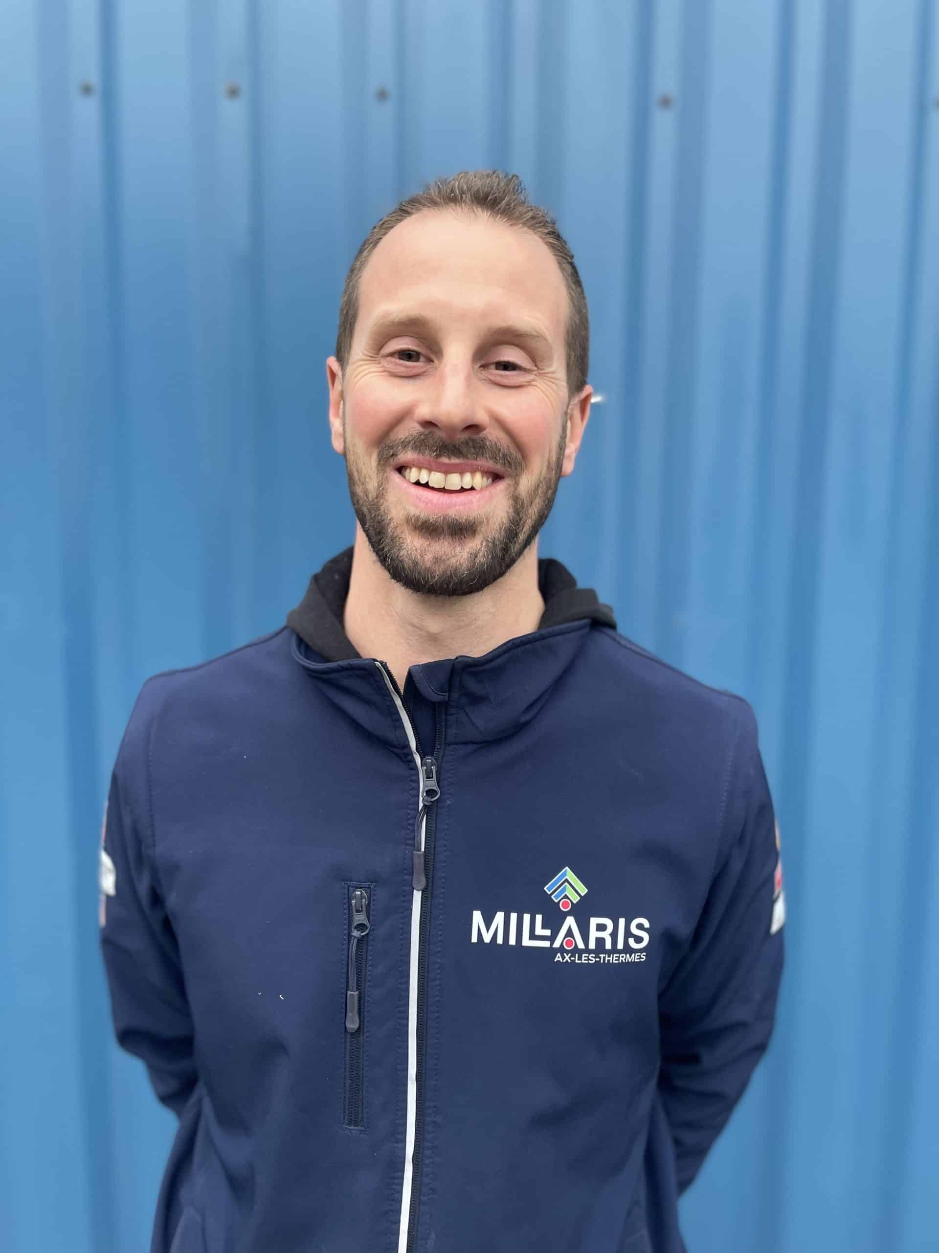 Portrait d’un homme souriant portant une veste bleue avec logo MILARIS, sur fond bleu.