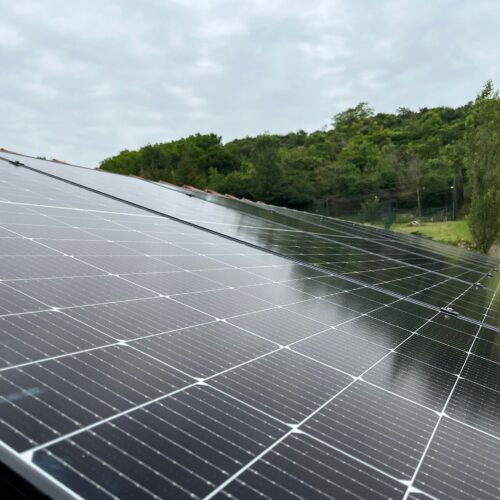 Panneaux solaires photovoltaïques installés sur le toit, avec une rangée de modules au premier plan et une végétation en arrière-plan sous un ciel nuageux.