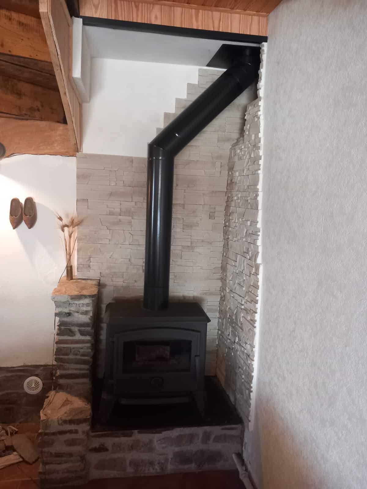 Poêle à bois noir encastré dans un mur de briques, avec conduit vertical et conduit courbé menant au plafond.