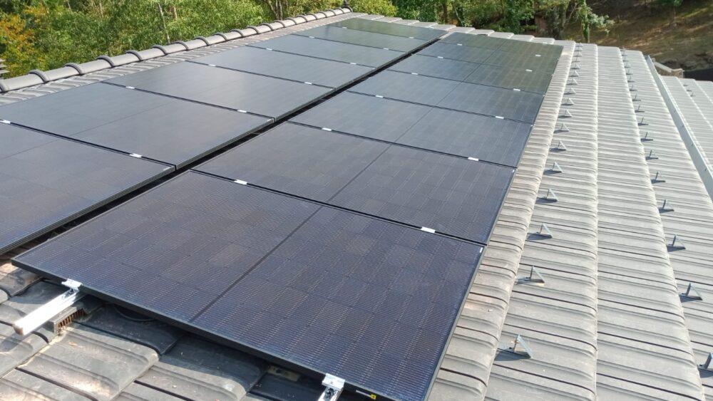 Toit d’un bâtiment recouvert de panneaux solaires photovoltaïques alignés sur plusieurs rangées, vus en perspective, avec des tuiles métalliques au second plan.