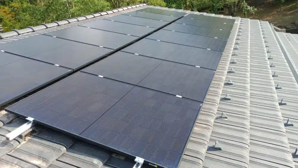 Toit d’un bâtiment recouvert de panneaux solaires photovoltaïques alignés sur plusieurs rangées, vus en perspective, avec des tuiles métalliques au second plan.