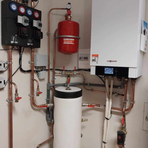Local technique de chauffage avec chaudière Viessmann, tuyauteries en cuivre, unité de régulation et capteurs, vase rouge et ballon d’eau chaude blanc.