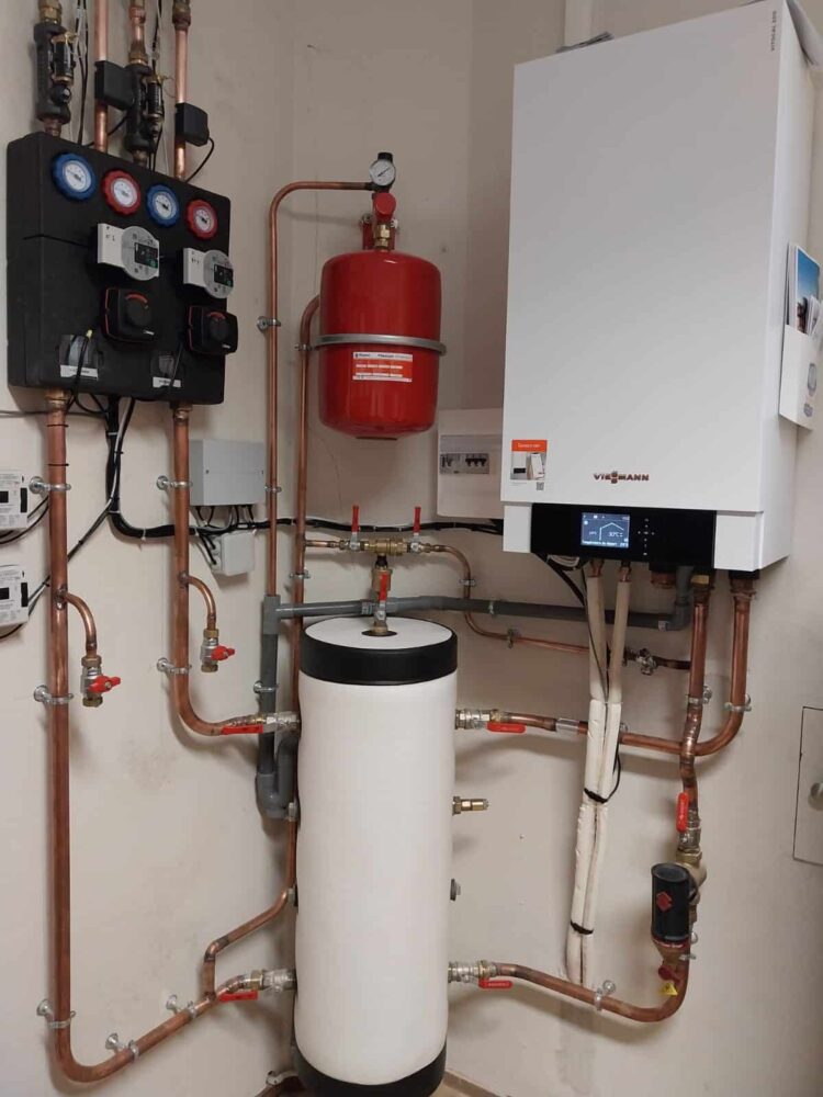Local technique de chauffage avec chaudière Viessmann, tuyauteries en cuivre, unité de régulation et capteurs, vase rouge et ballon d’eau chaude blanc.