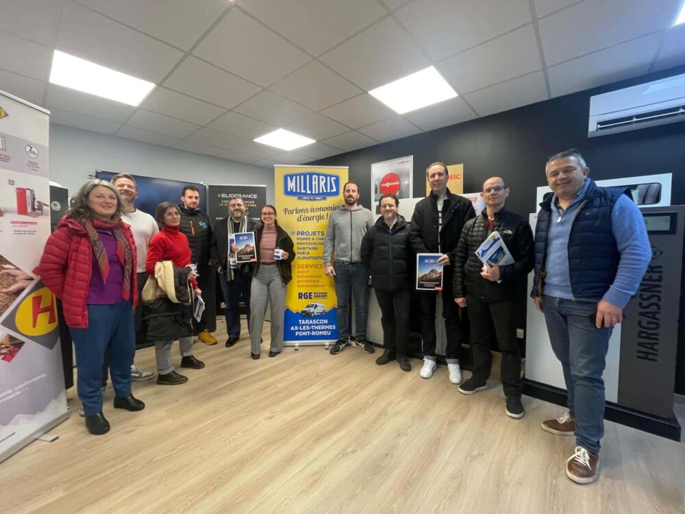 Photo de groupe dans un showroom : plusieurs personnes souriantes posent devant des stands, avec des panneaux “MILLARS” et des dossiers/plaquettes dans les mains.