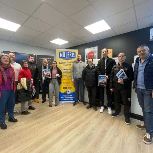Photo de groupe dans un showroom : plusieurs personnes souriantes posent devant des stands, avec des panneaux “MILLARS” et des dossiers/plaquettes dans les mains.