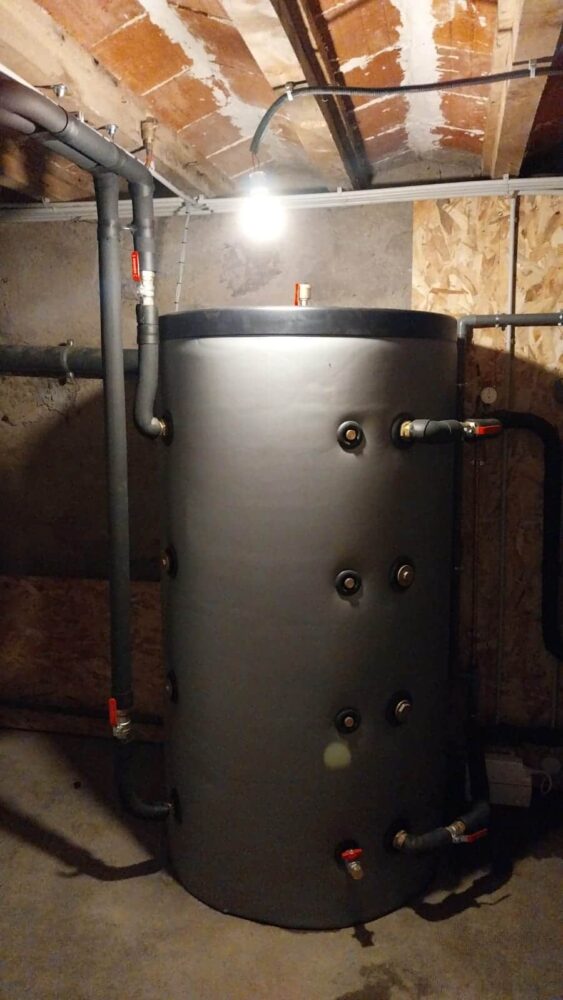 Chaudière noire industrielle installée dans une chaufferie, avec tuyauteries en métal et raccords au mur.