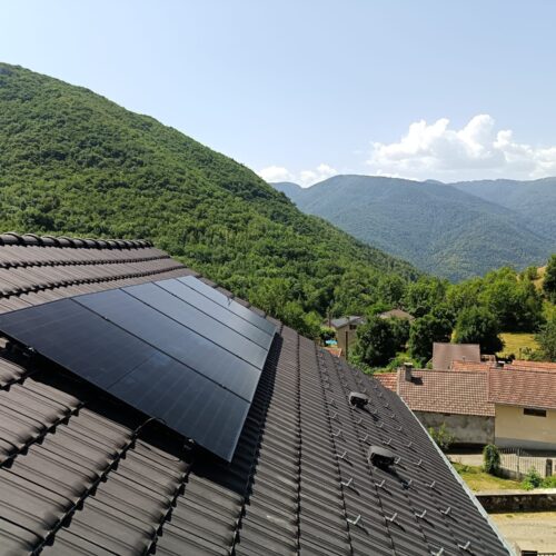 Toit d’une maison équipé de panneaux solaires, vue sur les collines et la vallée verdoyante sous un ciel bleu avec quelques nuages.