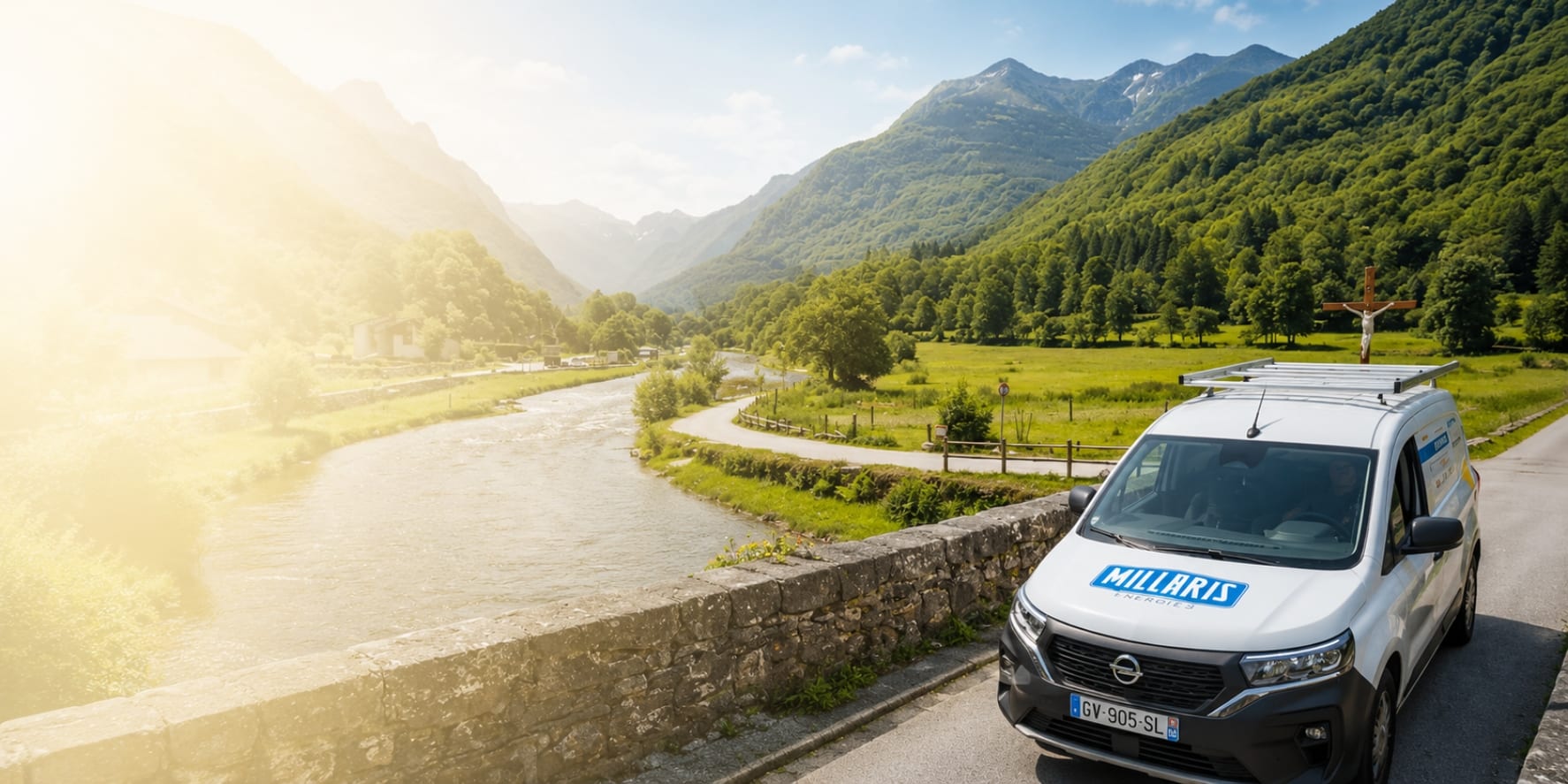 Camionnette de service « Millaris » garée sur une route au bord d’une rivière, avec des montagnes verdoyantes en arrière-plan et le soleil couchant.